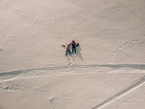 Aerial shot of two people making snow angels in the snow-covered landscape of winter.