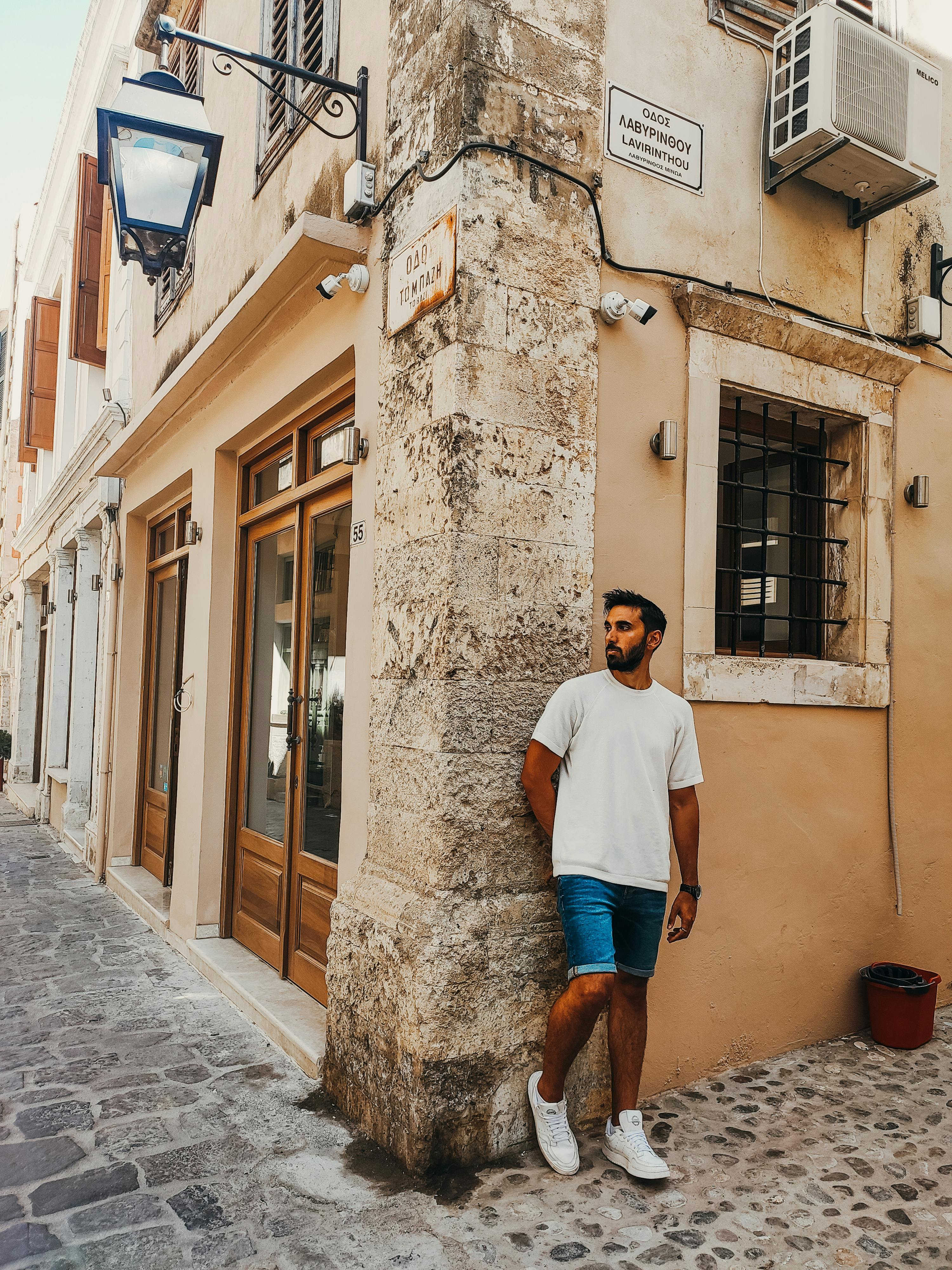 Free Man in a white shirt and denim shorts leaning on a building in Rethimno. Stock Photo