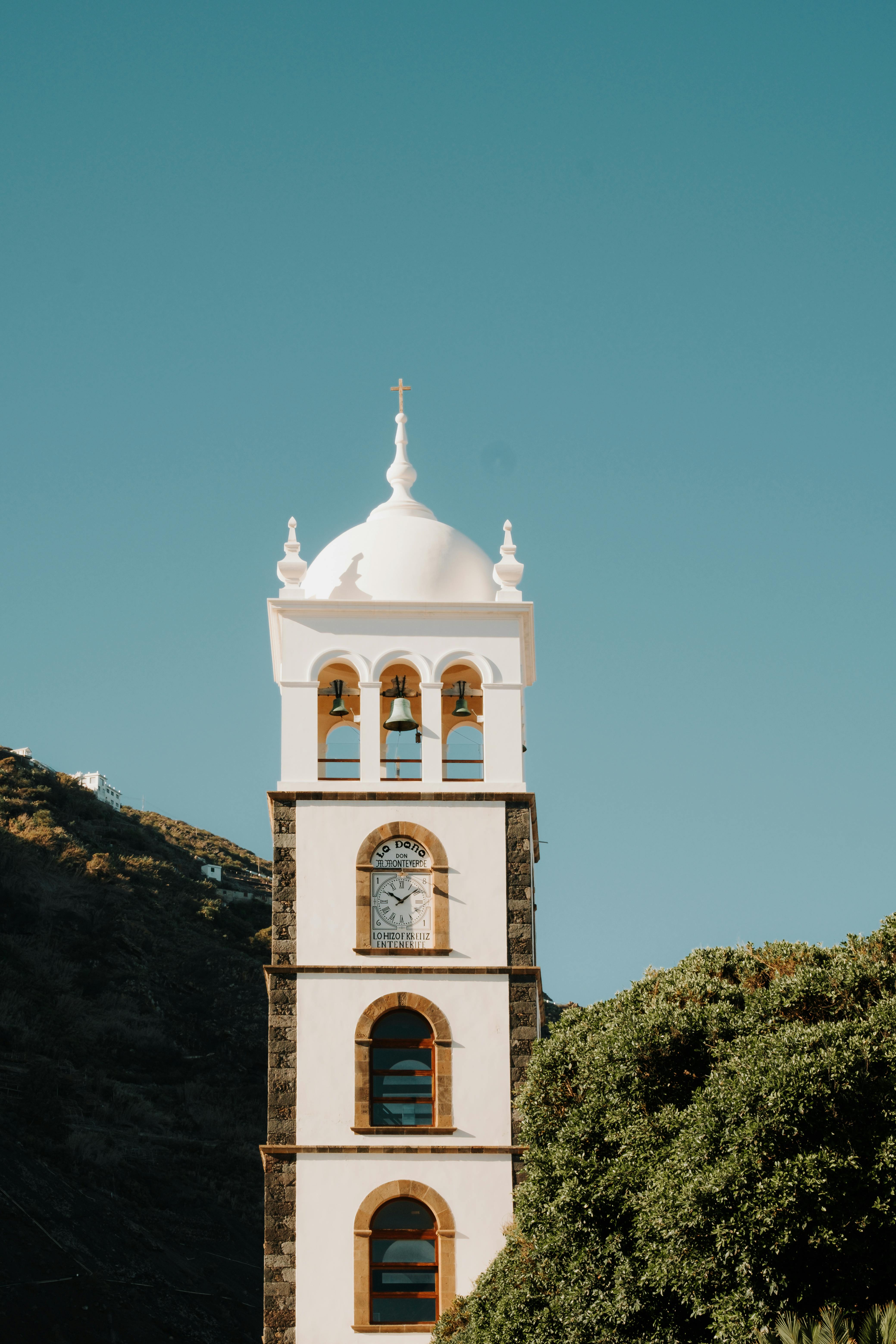 Vertical shot of a bell tower with white dome against a clear blue sky, showcasing vibrant contrast.
