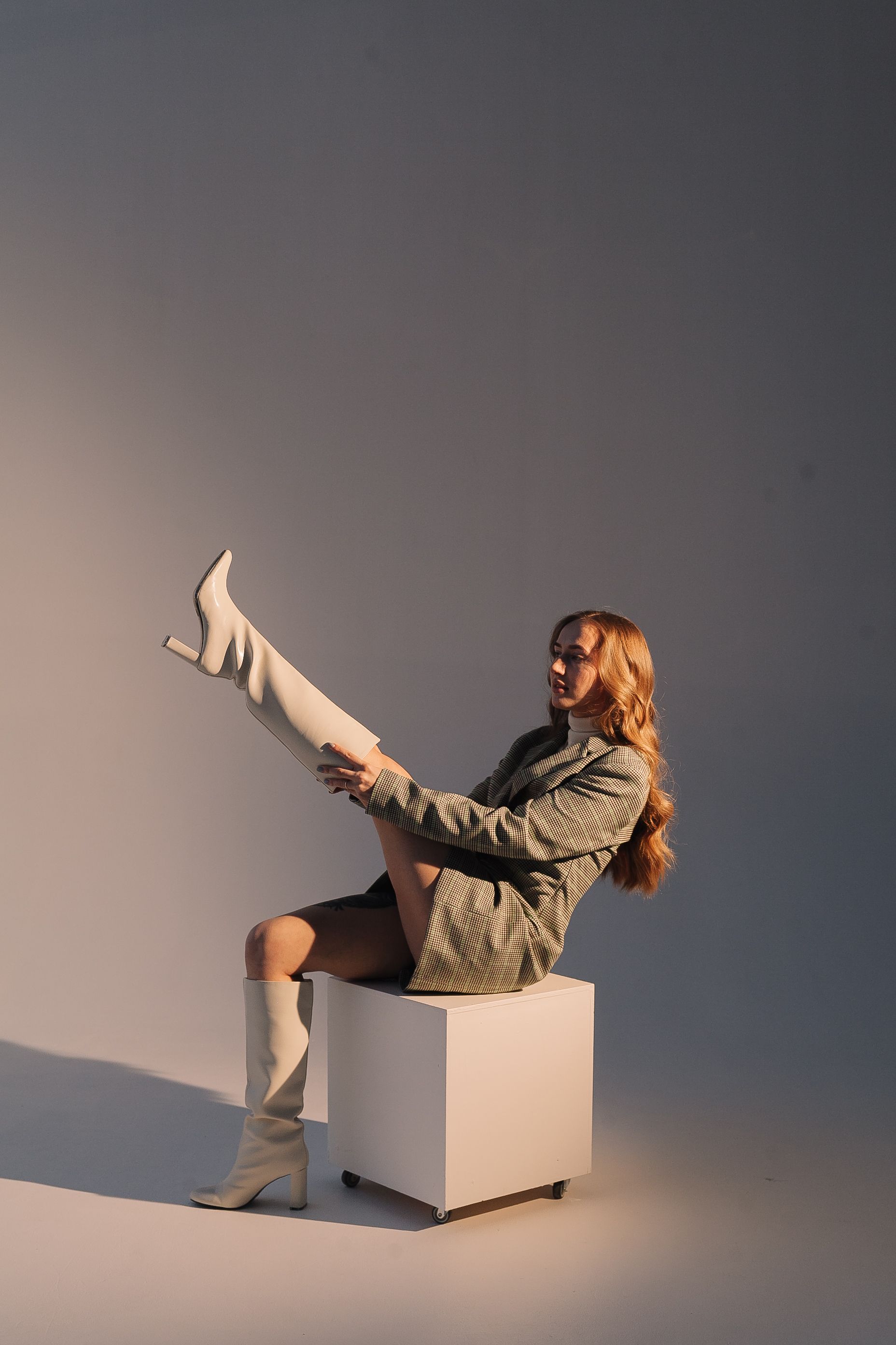 Mulher elegante posando em um estúdio com botas brancas e casaco formal.