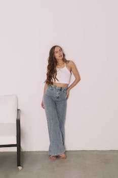 Woman with long wavy hair posing indoors in a casual outfit with jeans and a white top.