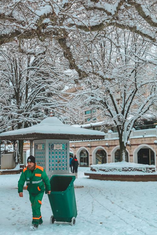 Free A janitor in green uniform works outdoors in a snow-covered public park during winter. Stock Photo