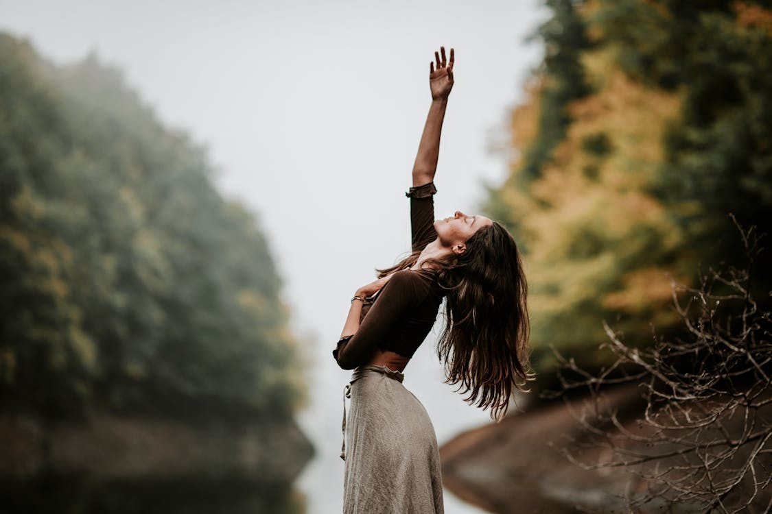 Free Woman with One Hand on Chest and Other Reaching to Sky Stock Photo