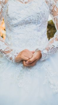 Close-up of a bride's hands in an elegant lace wedding gown, highlighting intricate details.