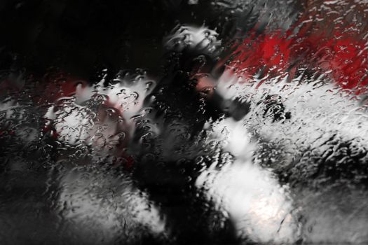 A close-up view of raindrops on a window, creating an abstract and artistic effect with blurred background colors.