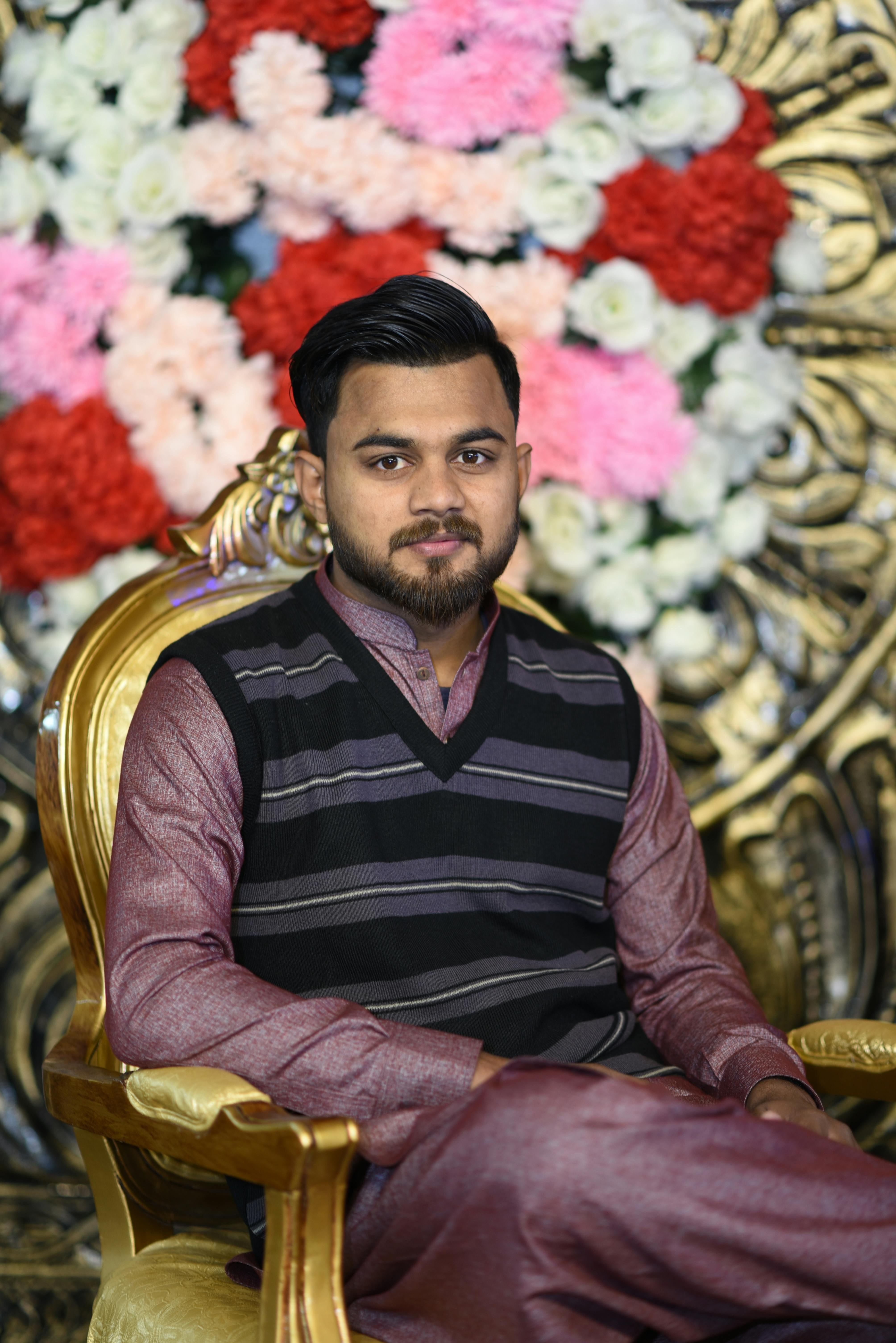 Portrait of a South Asian man seated on a gold chair with vibrant floral arrangement.