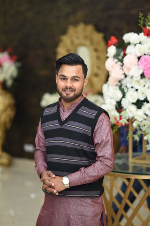 Free A smiling young man in traditional attire stands indoors, surrounded by floral decorations. Stock Photo