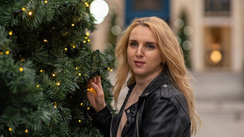 Woman in Black Leather Jacket Standing Beside a Christmas Tree
