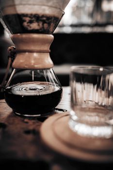 A close-up of brewed coffee in a Chemex with an empty glass on a wooden table, showing rich color and texture.