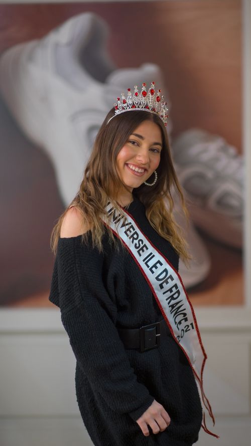 Free Young adult woman in black dress with crown and sash, smiling confidently in a portrait shot. Stock Photo