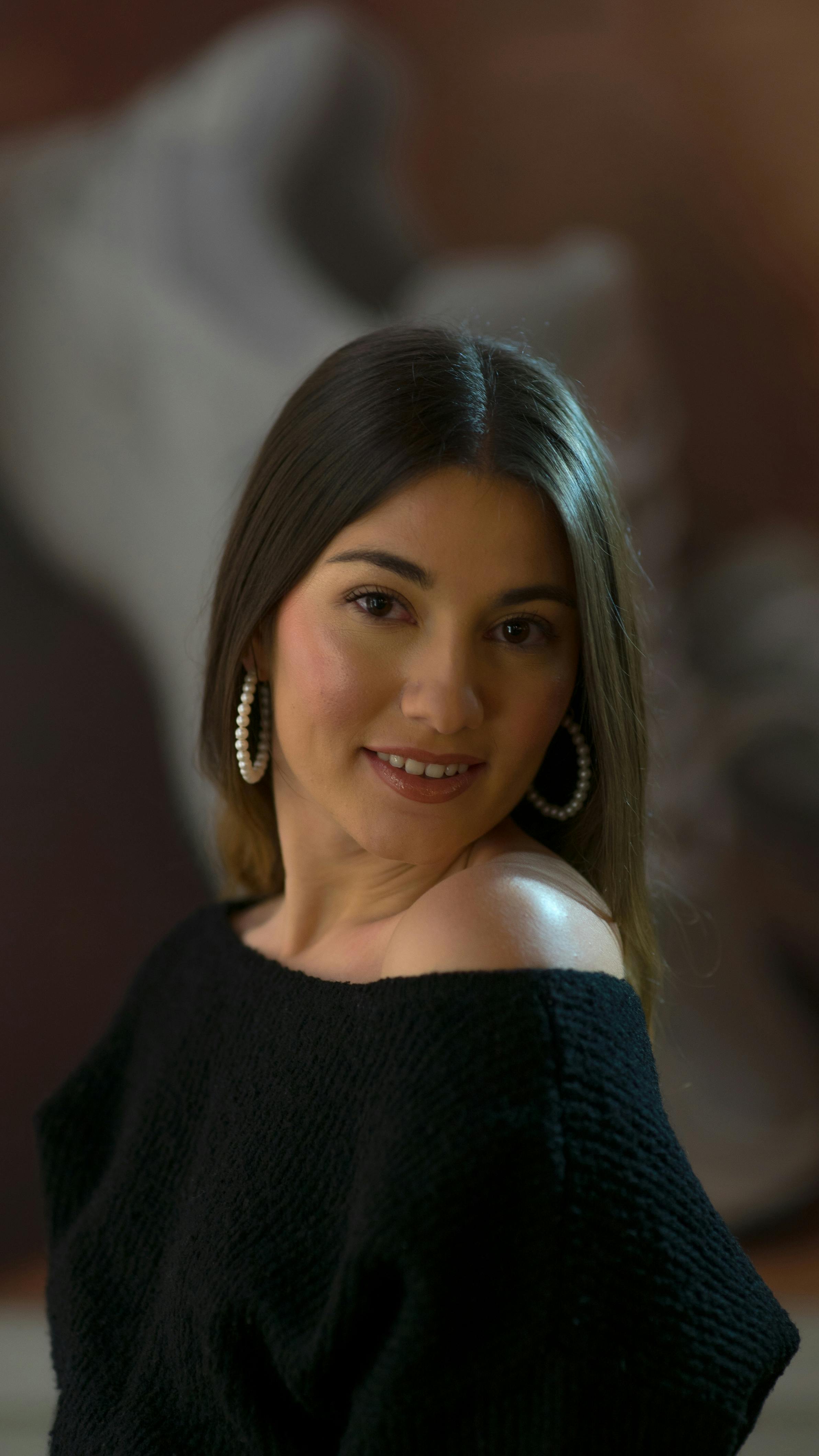 Portrait of a smiling woman in a black sweater and hoop earrings, showcasing elegance.