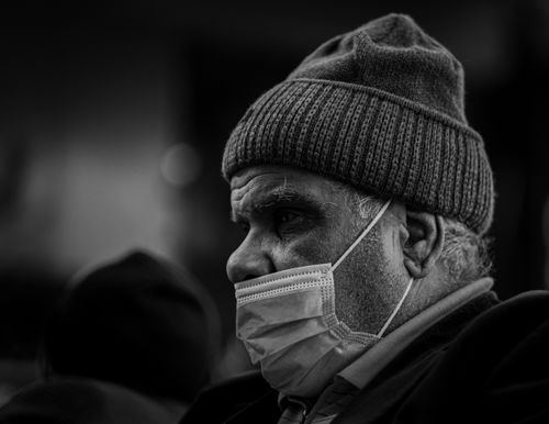 Free Close-up of an elderly man in a beanie wearing a face mask, captured in monochrome. Stock Photo