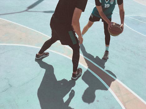 Close-up of two athletes playing basketball outdoors on a sunny day.