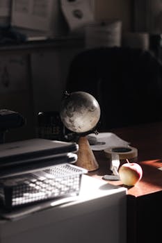 A cozy office desk scene with a globe, apple, and papers in warm sunlight.