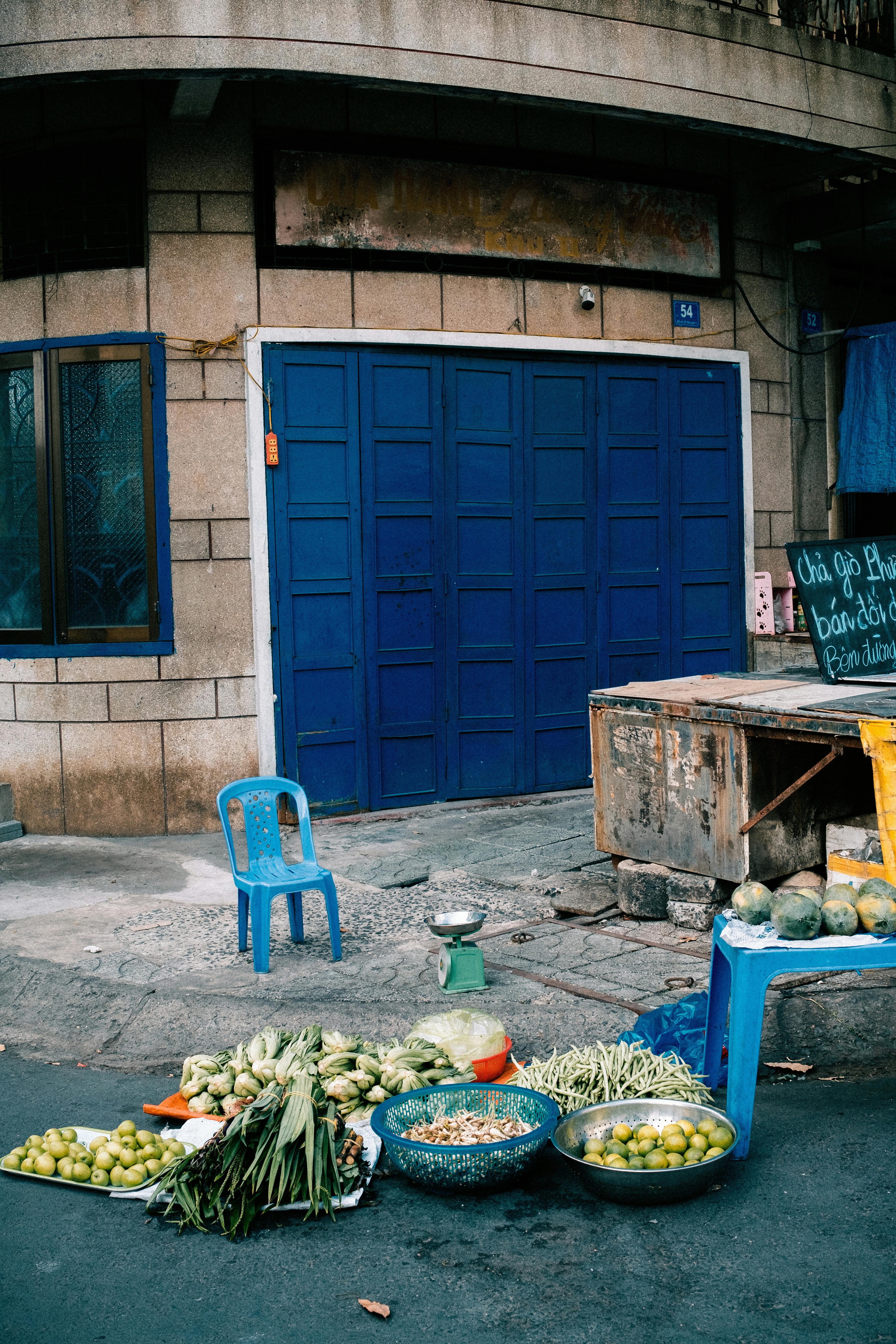 Street market display of fresh vegetables outside blue doorway in urban setting.