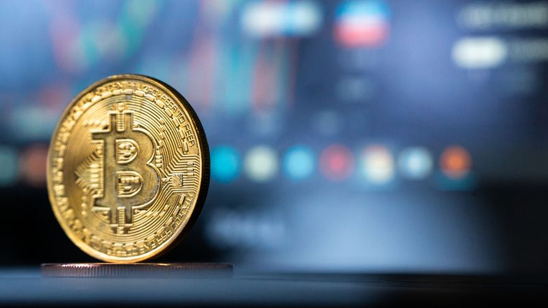 Gold Bitcoin coin with blurred financial chart in background, representing cryptocurrency trading.