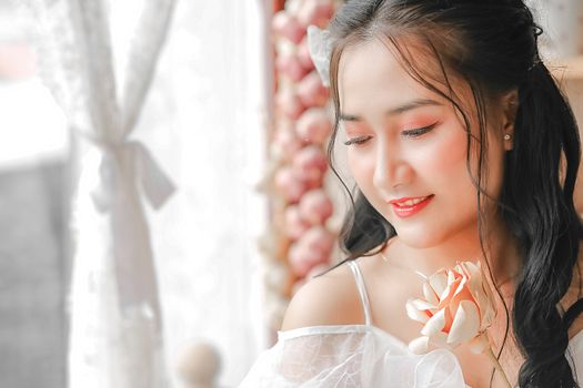 Asian woman holding a flower by a window, exuding elegance and tranquility.