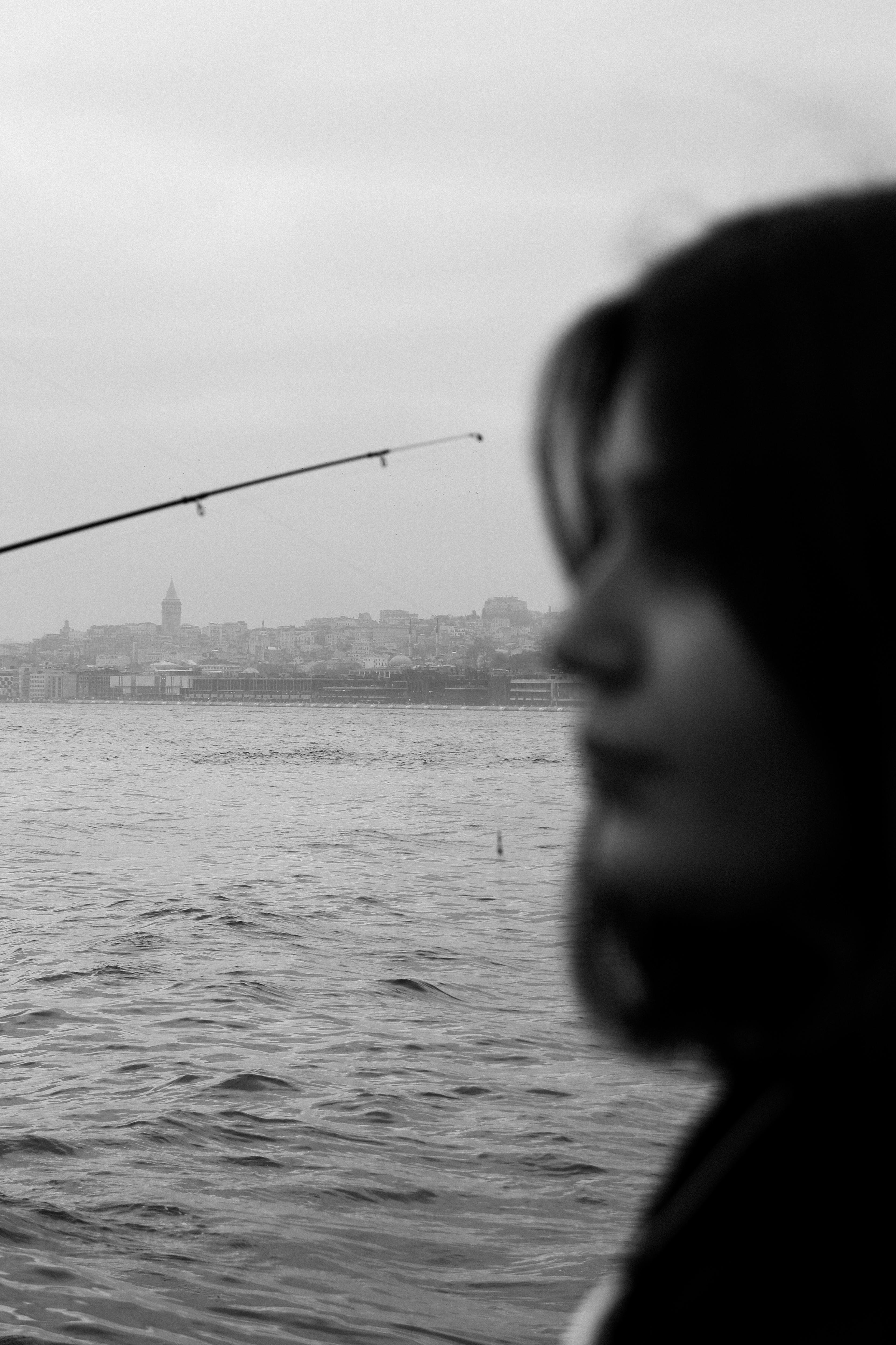 Black and white photo of a woman in profile by the water with a cityscape in the background, creating a serene mood.