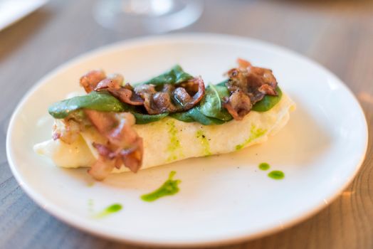 Savor this mouth-watering omelette topped with crispy bacon and fresh spinach leaves on a ceramic plate.