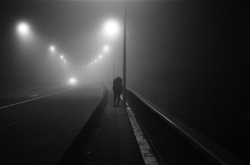 Free A solitary person walks across a foggy bridge at night, illuminated by streetlights. Stock Photo
