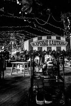 Black and white photo of a food cart with festive lights at a market.