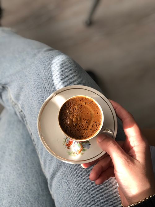 Free Person holding coffee cup with frothy coffee in a relaxed, cozy atmosphere. Stock Photo