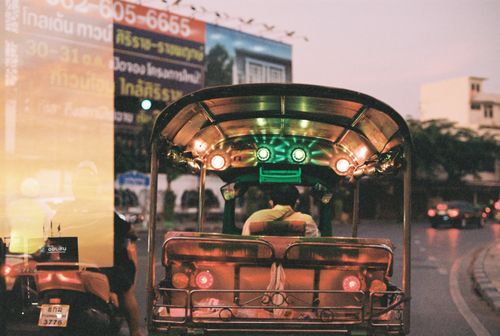 Free A colorful tuk-tuk drives through the streets of Bangkok during sunset, capturing the city's lively atmosphere. Stock Photo