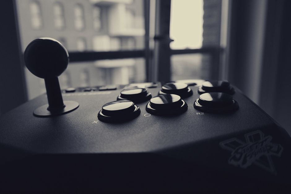 Black and white close-up of a retro gaming joystick with cityscape background.