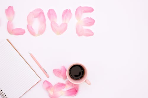 Love Spelled with Pink Flower Petals Near a Cup of Coffee