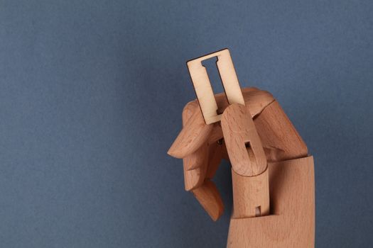 Wooden mannequin hand holding a razor blade against a blue background, conveying danger and safety themes.