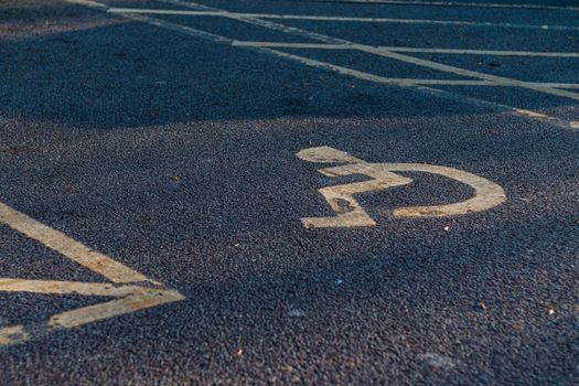 Yellow wheelchair symbol marking on asphalt in a parking lot.
