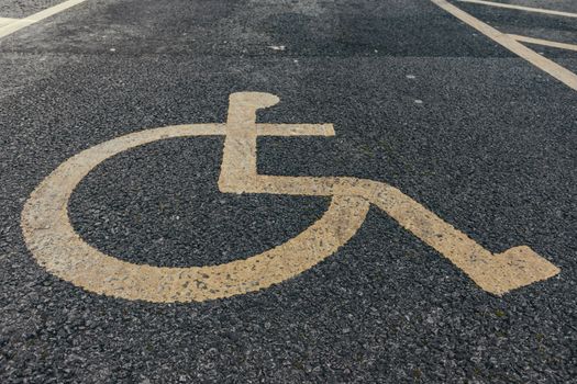 Close-up of a painted accessibility symbol on asphalt parking pavement.
