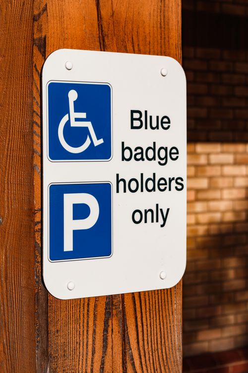 Free A blue badge parking sign mounted on a wooden post indicating reserved parking for disabled access. Stock Photo