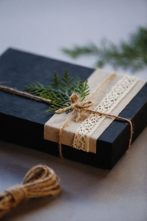 Free Black gift box wrapped with twine and lace, accented with a green leaf. Stock Photo