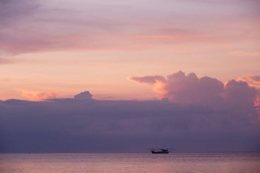 A picturesque view of the ocean with a silhouetted ship against a pink sunset sky.
