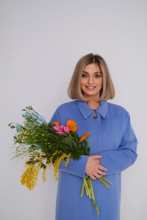 Free Pretty Blond Woman in Blue Coat Standing with Armful of Wild Flowers Stock Photo