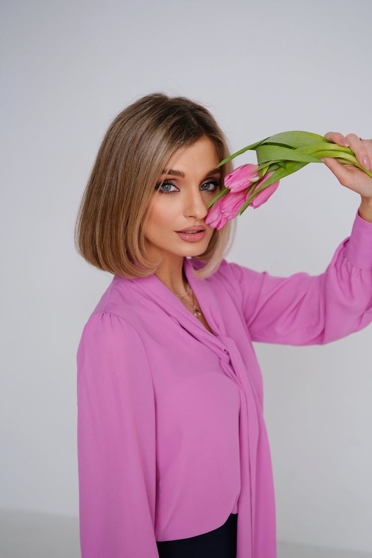 Woman In Pink Shirt Touching Her Face With Pink Flowers