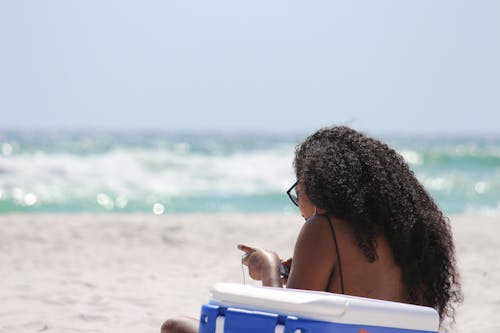 Woman Sitting on Sand Beside Blue and White Cooler Box Near Shore