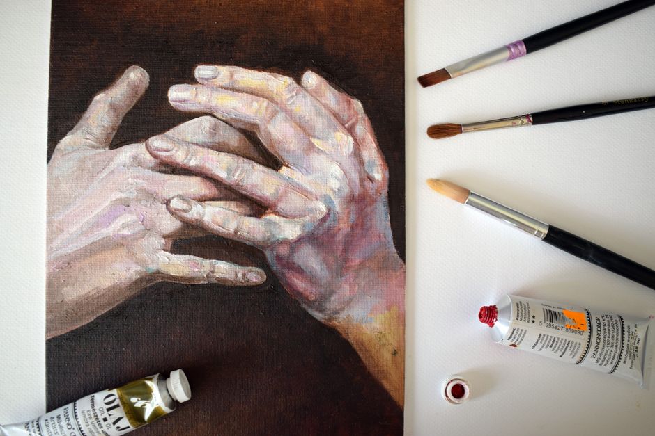 Mano che dipinge con il pennello tra tubetti di colore a olio