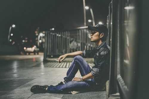 Free Man sits on the city street at night, smoking against an urban backdrop. Stock Photo