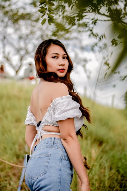 Woman in White Crop Top and Blue Denim Jeans Standing on Grass