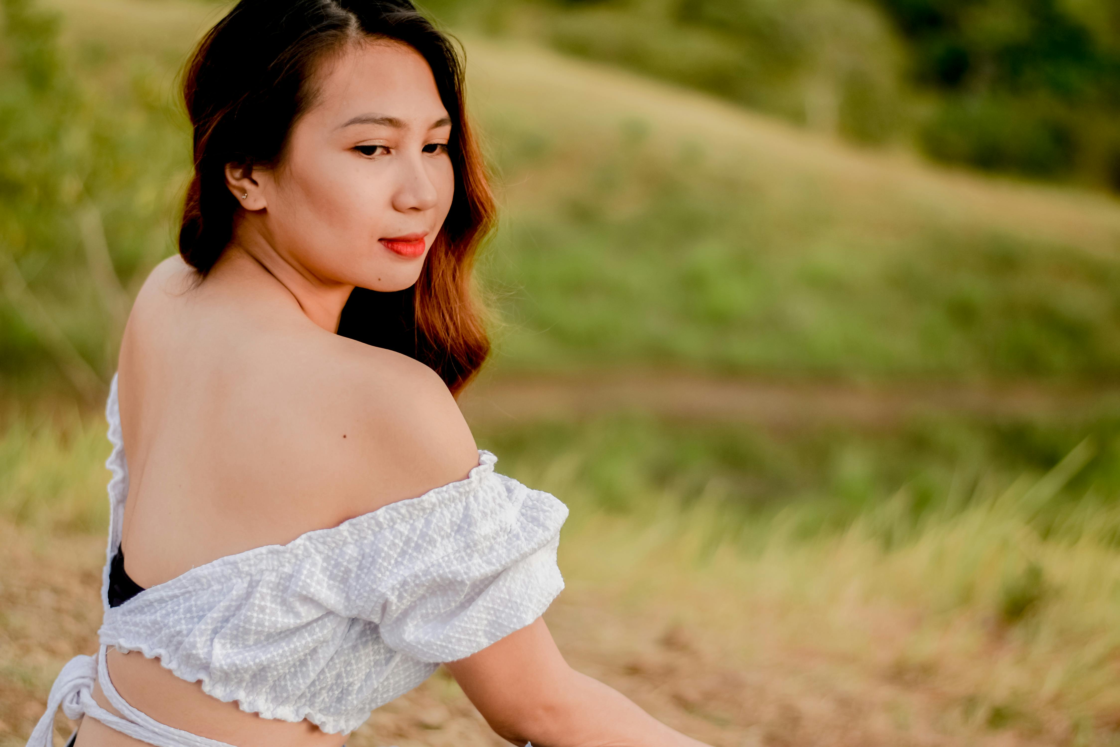 A woman in off-shoulder attire poses gracefully in a lush, green outdoor setting.
