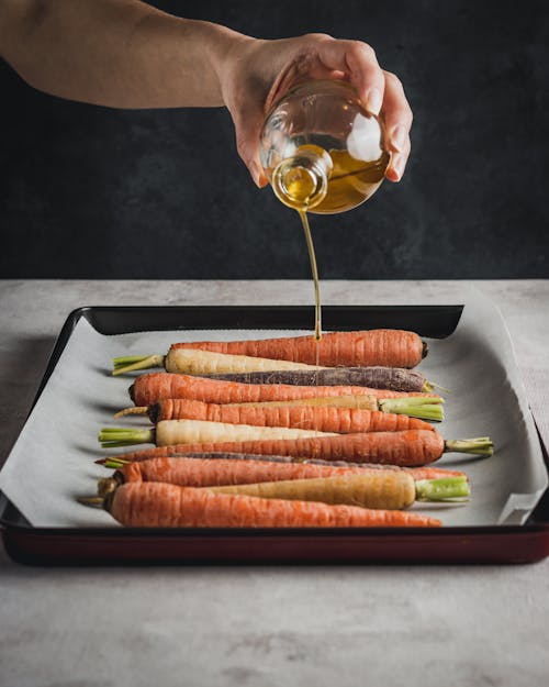Person Pouring Olive Oil on Fresh Carrots