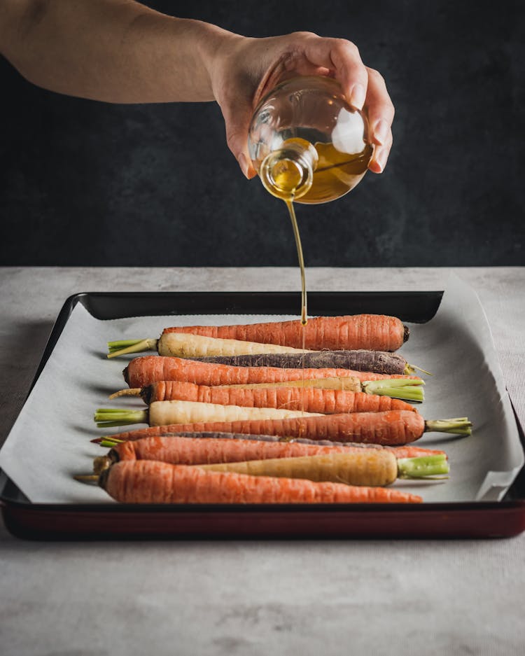 Person Pouring Olive Oil On Fresh Carrots