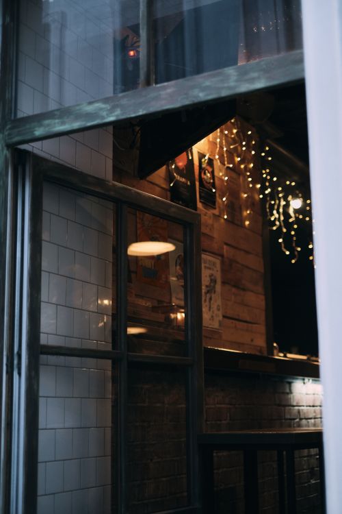 Free View through a window into a rustic cafe interior with string lights and wooden decor. Stock Photo