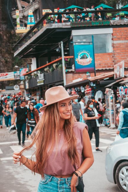 Smiling woman with fedora in bustling Peñol street, Colombia, showcasing urban lifestyle.