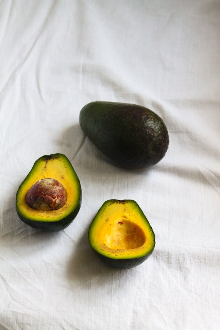 Two Ripe Avocado Fruits And One Cut In Halves
