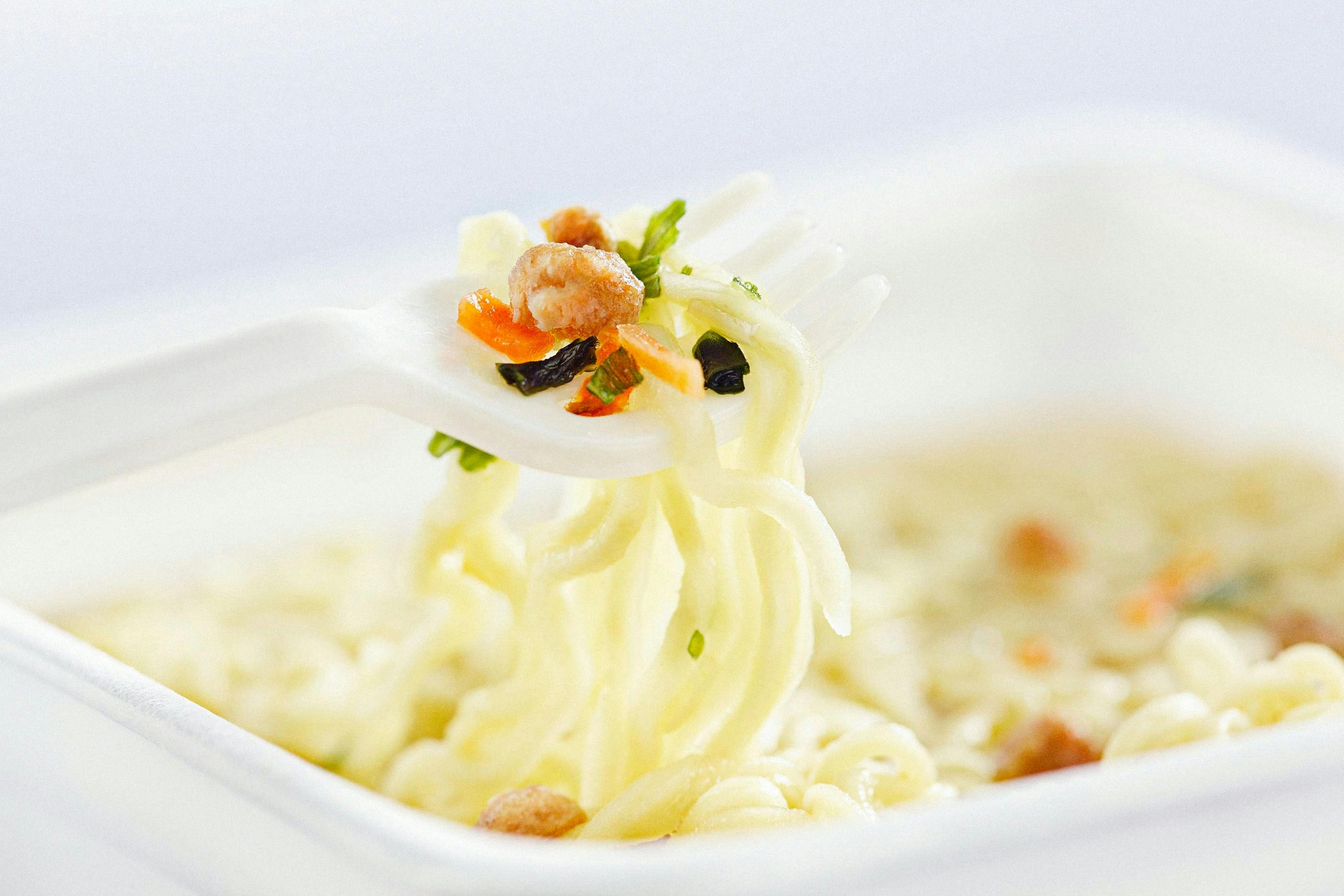 Delicious forkful of instant noodles with vegetables in white bowl, perfect meal on the go.