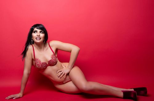 Free A confident woman poses in red lingerie on a vibrant red background, creating a striking studio image. Stock Photo