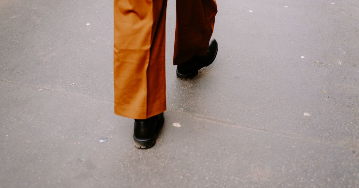 Close-up walking scene with black shoes and brown pants on a city street.